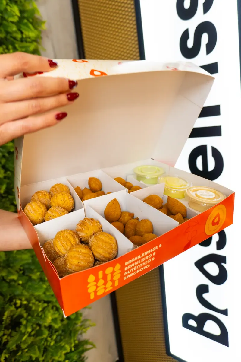 Caixa aberta com coxinhas, salgados e molhos