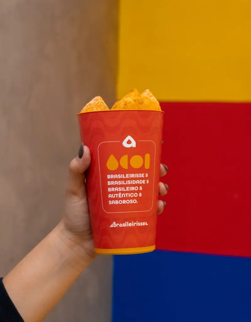 Mão segurando um copo vermelho Brasileirisse com coxinhas